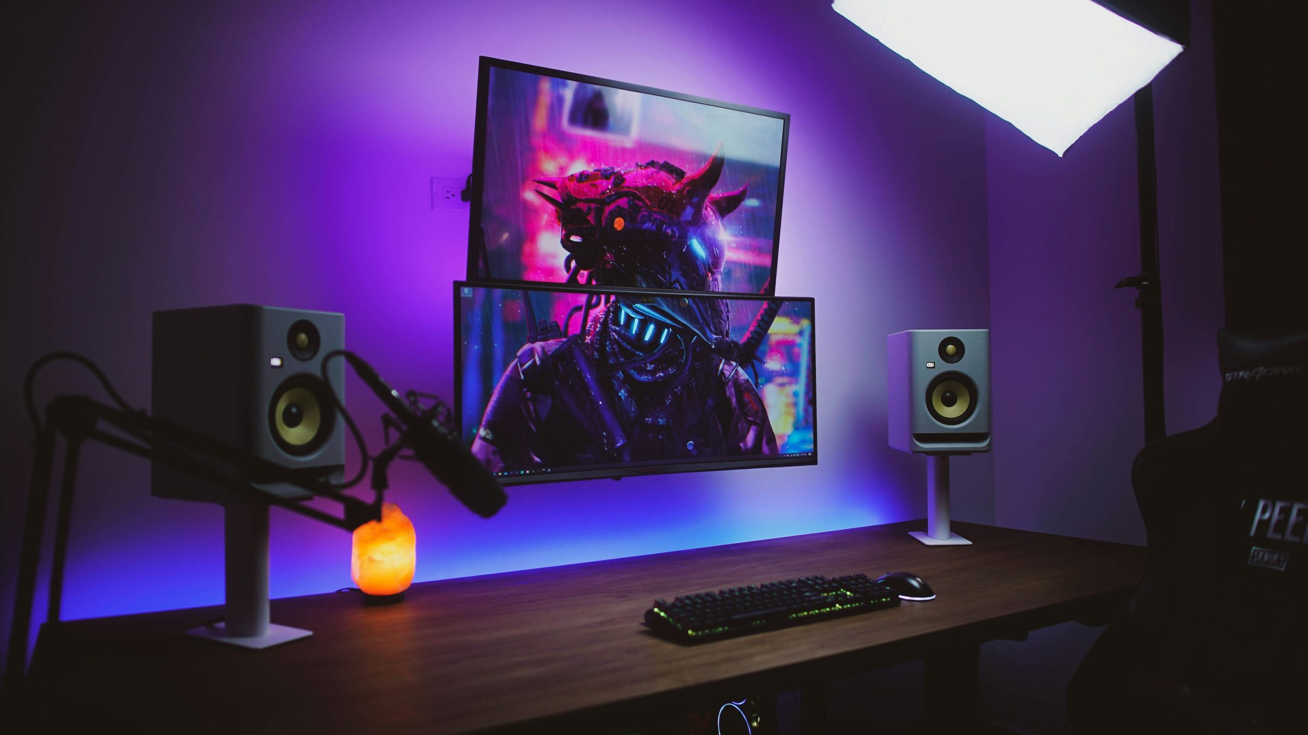 Purple-lit desk with stacked monitors, studio speakers, and a microphone